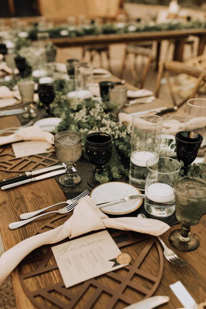 Long wood wedding head table with eucalyptus layered in center and candles.
