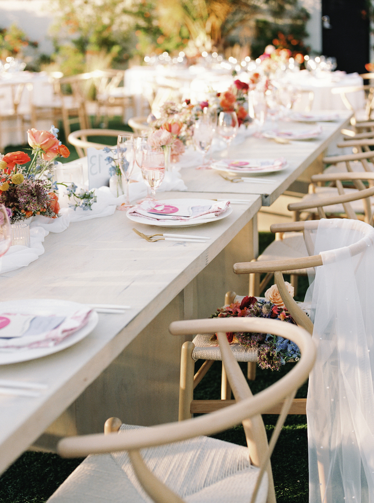 Long wedding reception table with place settings of white with pink accents.