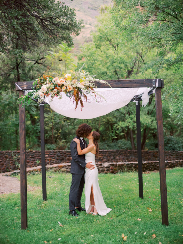 Bride and groom kissing under square wedding ceremony arch.