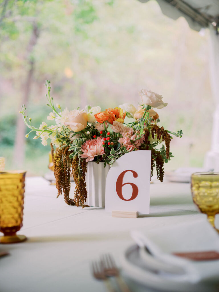 Wedding reception centerpiece of short flowers with table number in front of it.
