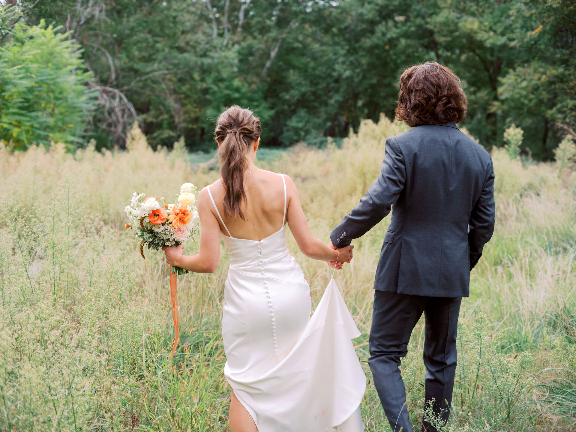 Bride and groom holding hands walking away in long grass field in Sedona.