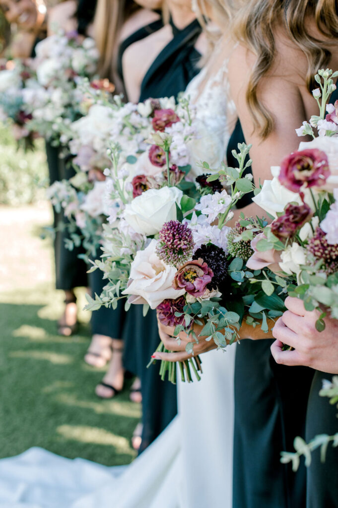Bride and bridesmaids holding bouquets of white and mauve flowers.