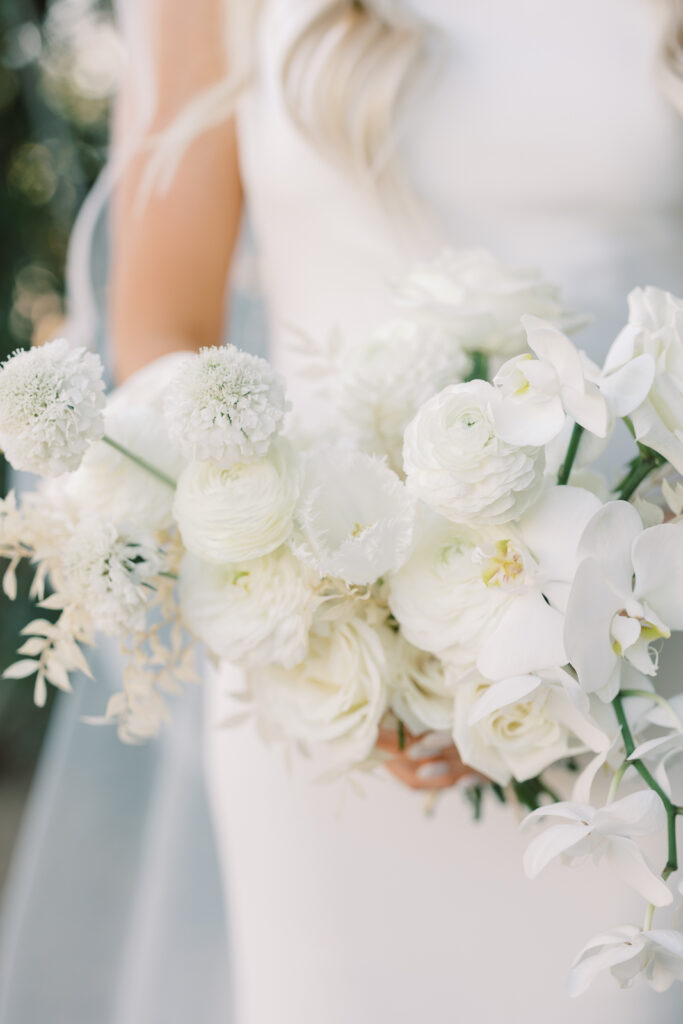 White flowers wedding bouquet with bride in white dress behind it.