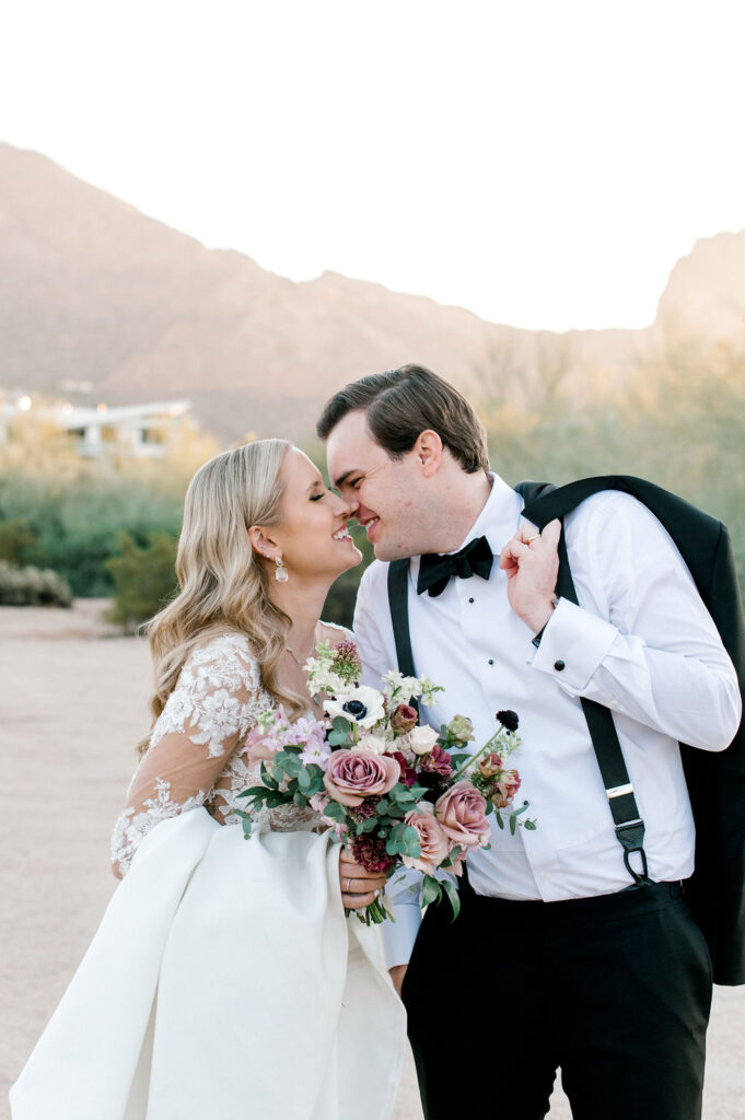 Bride and groom standing in desert landscape with noses touching, smiling.