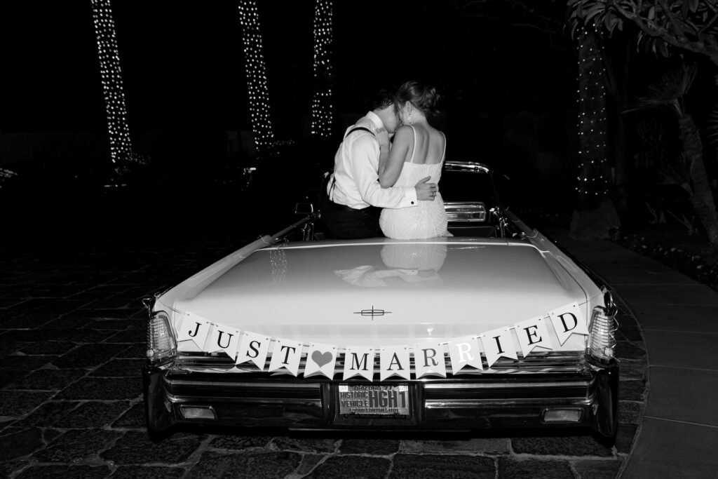 Couple sitting on trunk of vintage car embracing.