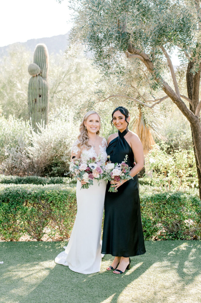 Bride standing with bridesmaid in dark green dress in desert landscape.