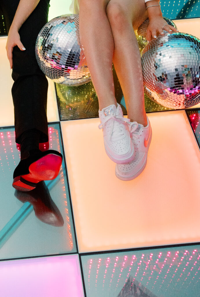 A man and woman's feet on a dance floor with disco balls on the ground.
