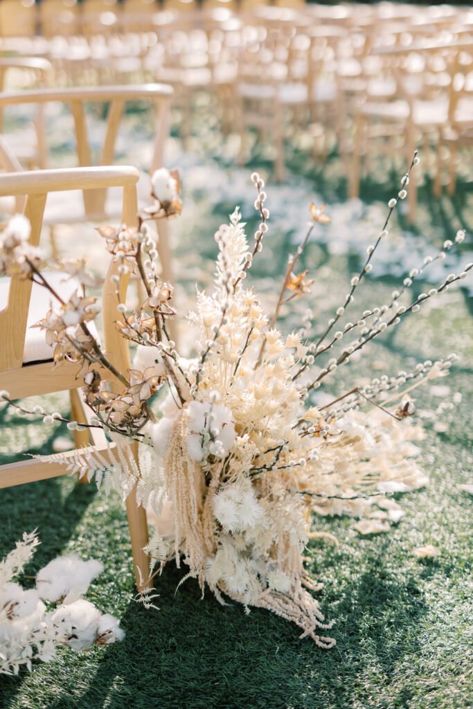 Dried floral arrangement of white and tan flowers on the ground behind the wedding ceremony chairs.