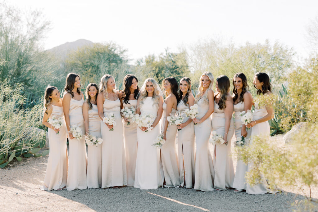 Ladies holding bouquets standing in a row with desert trees around them.