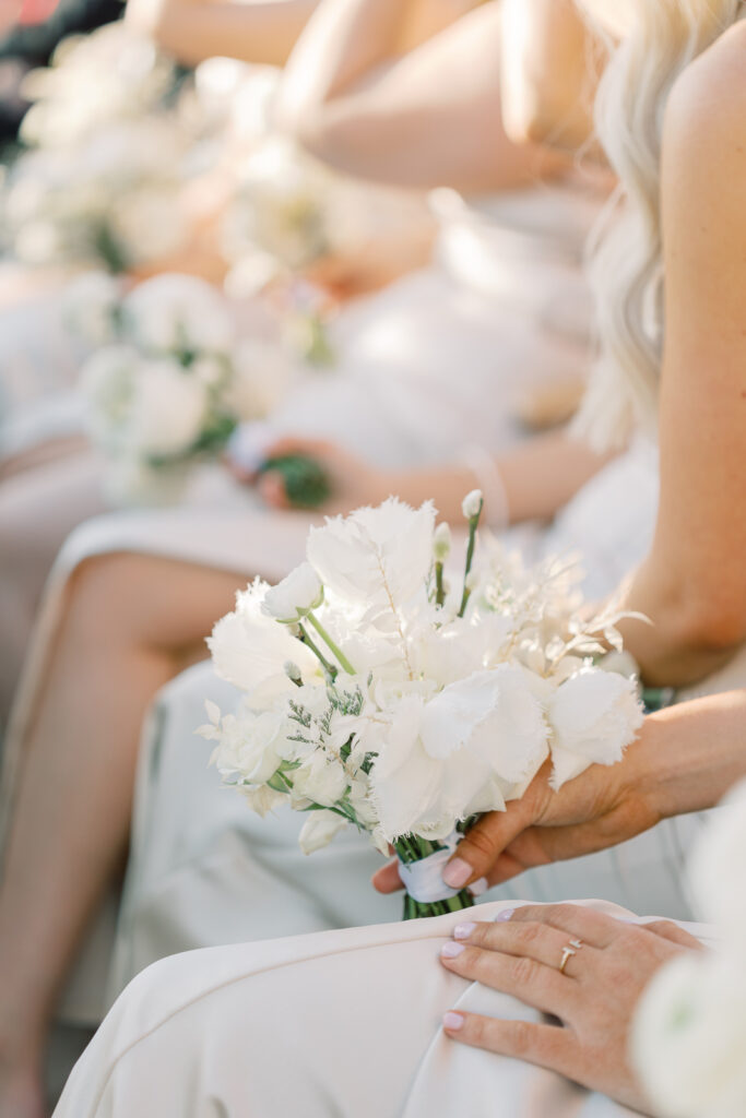 Woman sitting down in a row with bouquets of white flowers in their hands.