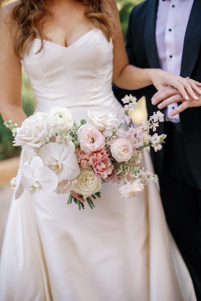 Bride resting hand on groom's, holding bridal bouquet of white and pink flowers.