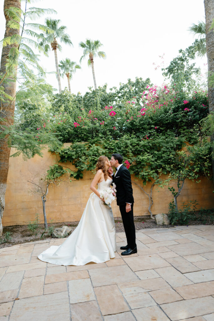 Bride and groom kissing in landscaped tile area at Royal Palms.