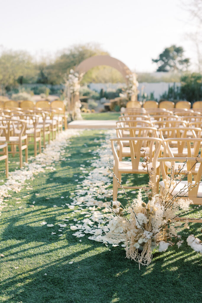 A wedding ceremony with tan chair for guests and white rose petals down the aisle.