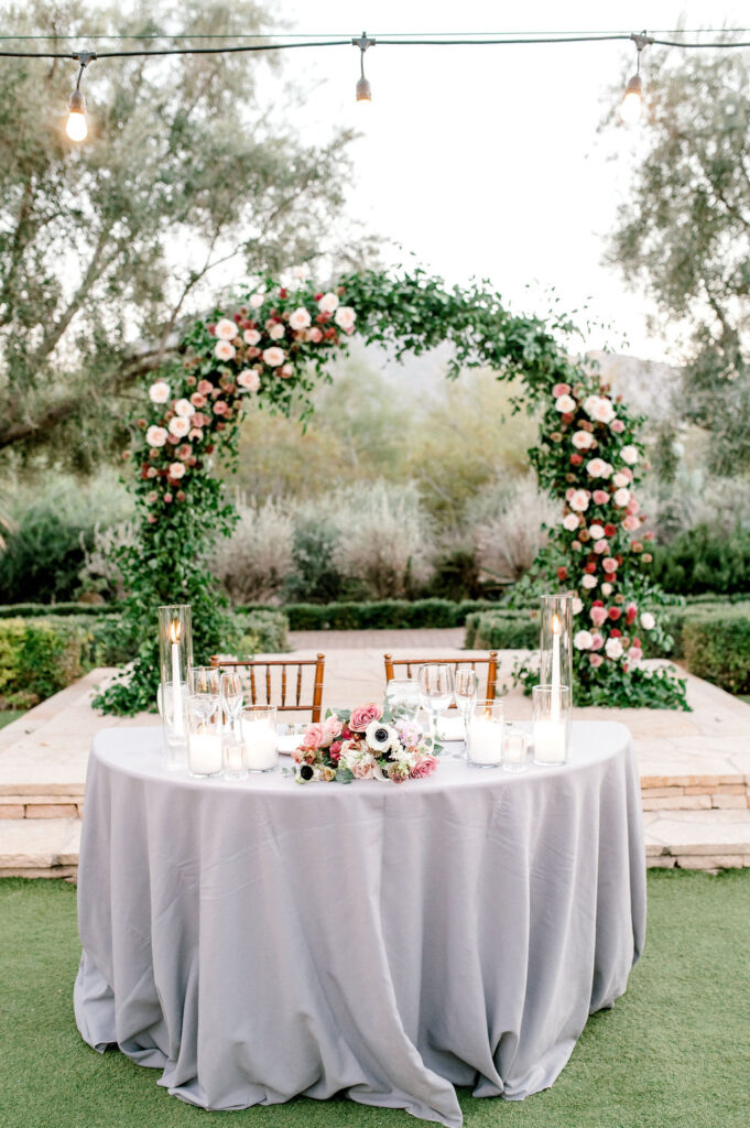 Wedding ceremony arch at altar with greenery and floral installed on it with sweetheart table in front of it.