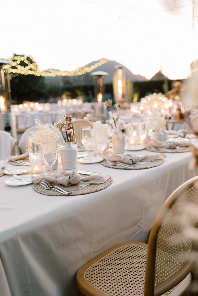 Outdoor wedding reception with chairs and white clothed tables with a bunch of candles on them.