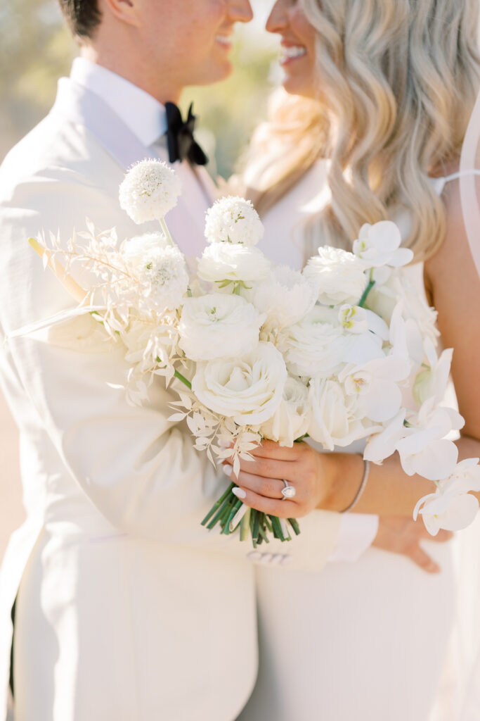 Woman and man embracing with woman holding white flowers bouquet included roses, ranunculus, and orchids.