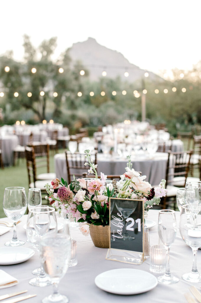 Outdoor reception space with round tables with flower centerpieces.
