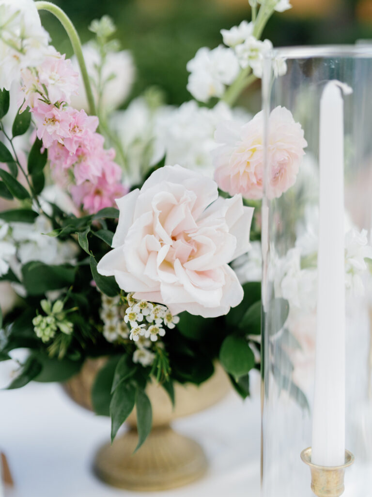 Close up of reception centerpiece with candles and flower arrangement in gold vase of white and pink flowers.