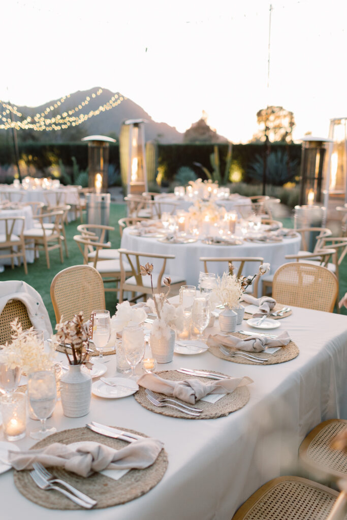 A fancy outdoor wedding reception with many chairs and a lot of centerpieces and lights and candles everywhere.
