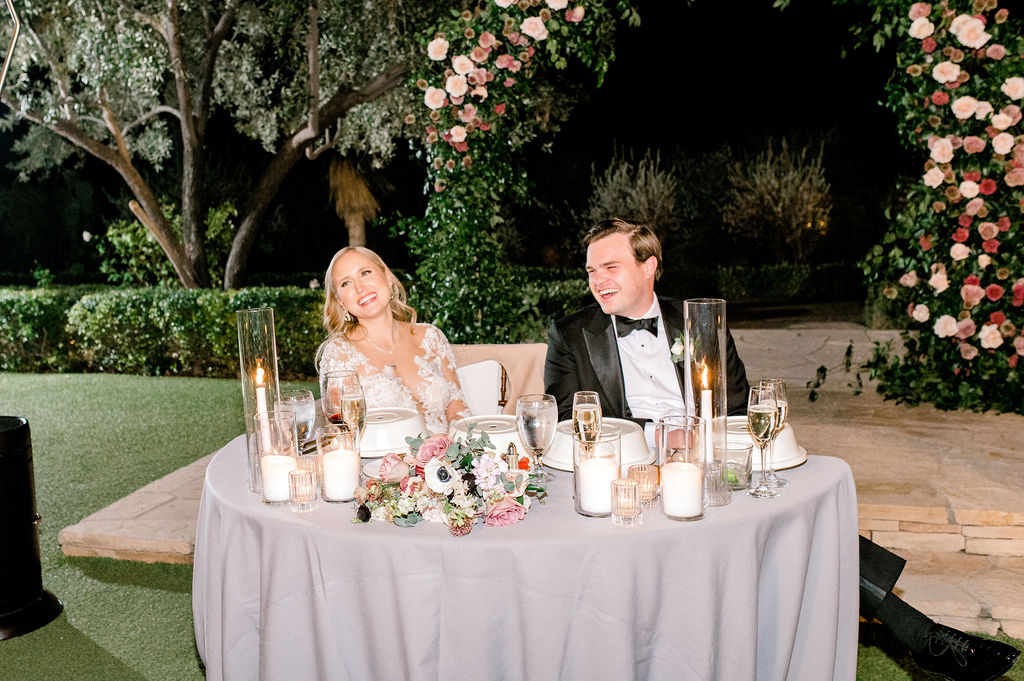 Bride and groom laughing, sitting at sweetheart table.