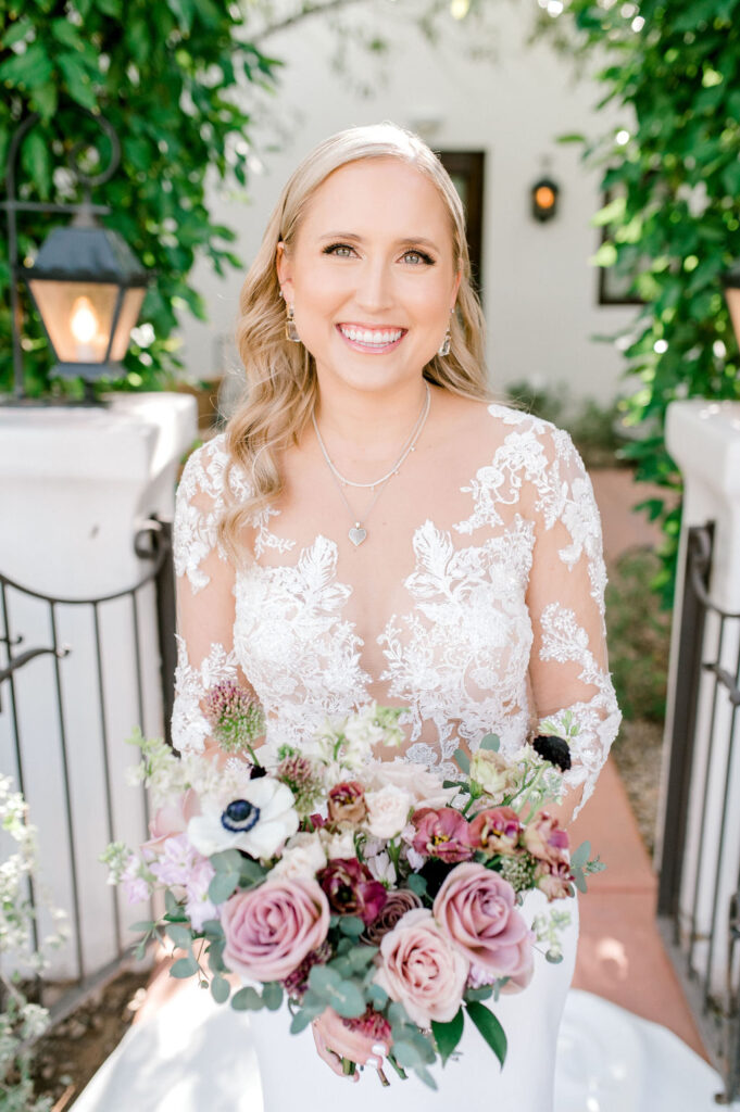 Bride holding bouquet of pink, white and mauve flowers, smiling.