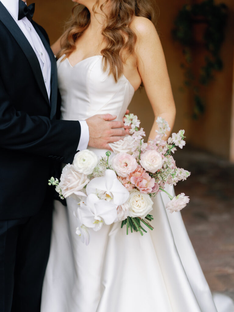 Bride and groom embracing with bride holding bouquet of white and blush pink flowers.