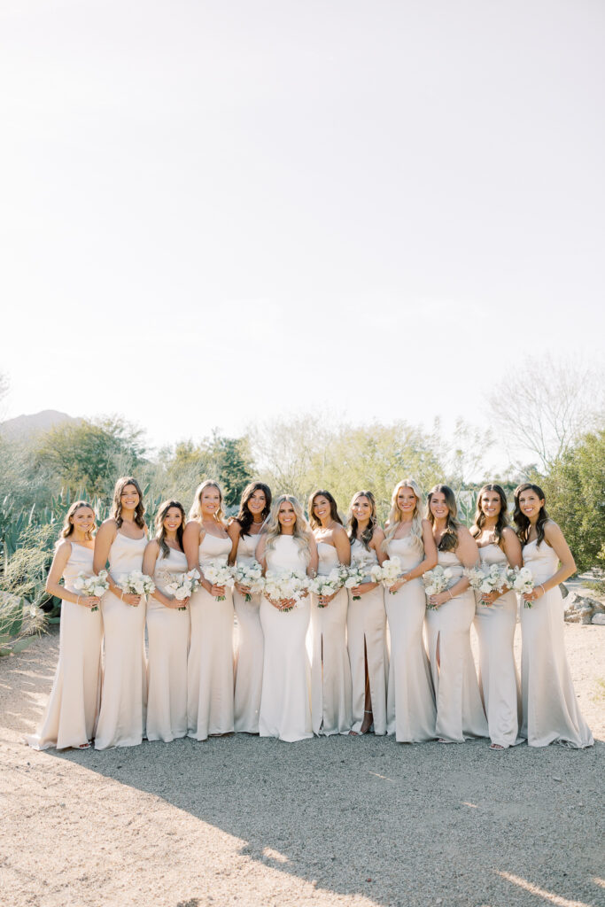 Ladies holding bouquets standing in a row with desert trees around them.