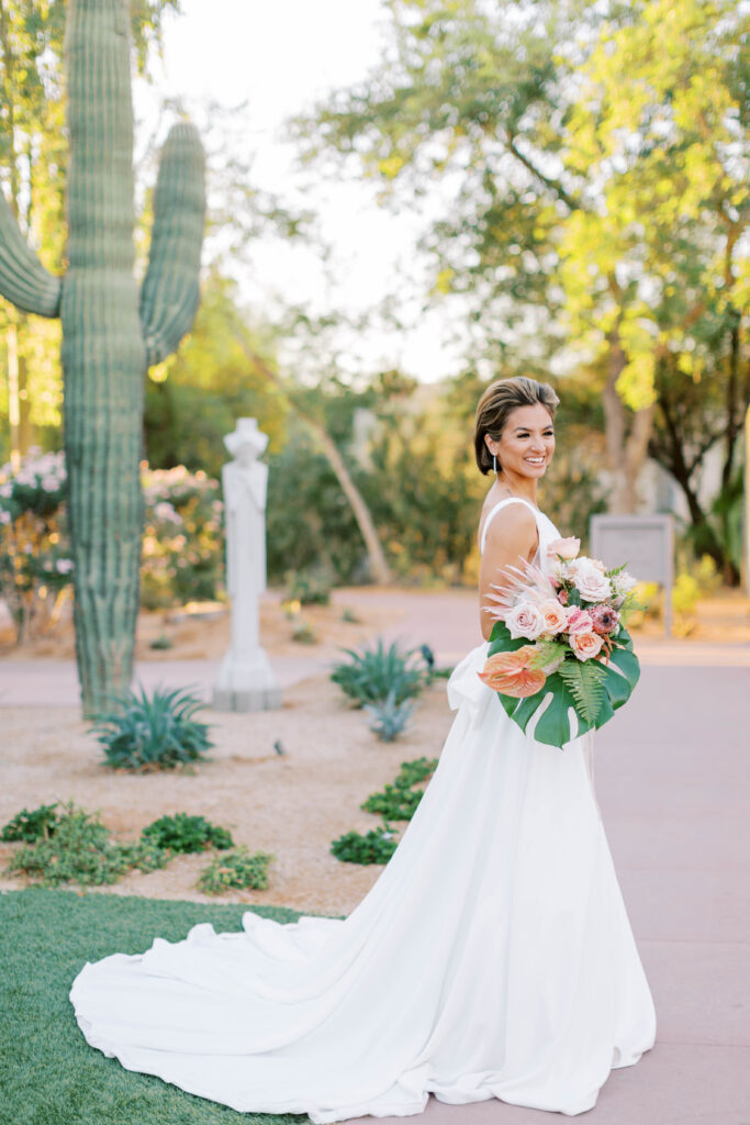 Bride holding large tropical bouquet with monstera leaf and protea in desert setting.