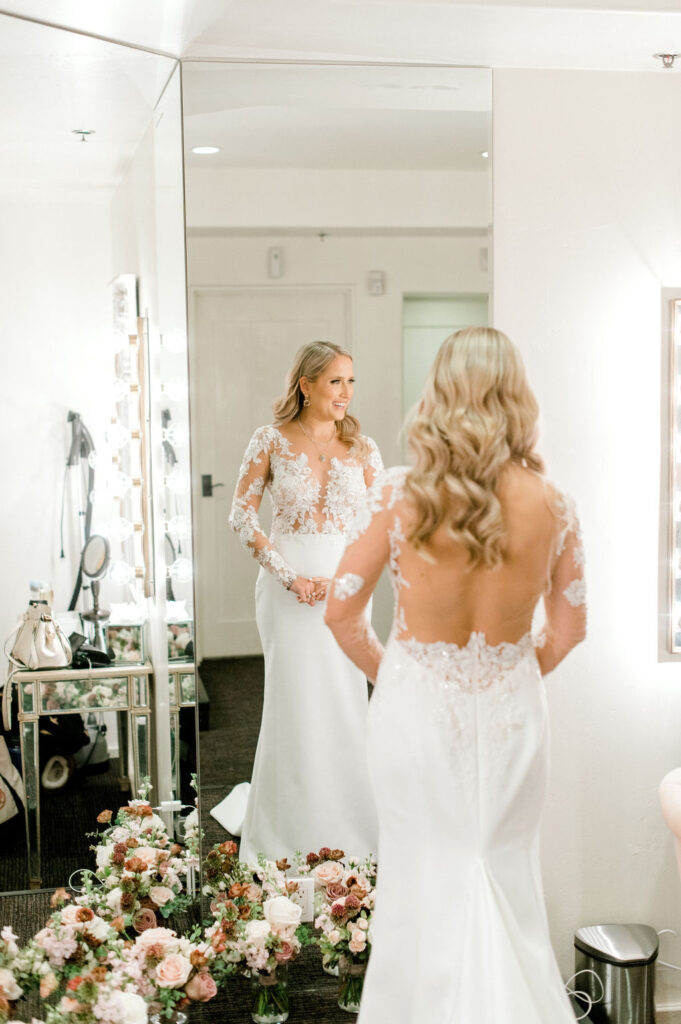 Bride in dressing room in front of floor length mirror in wedding dress.