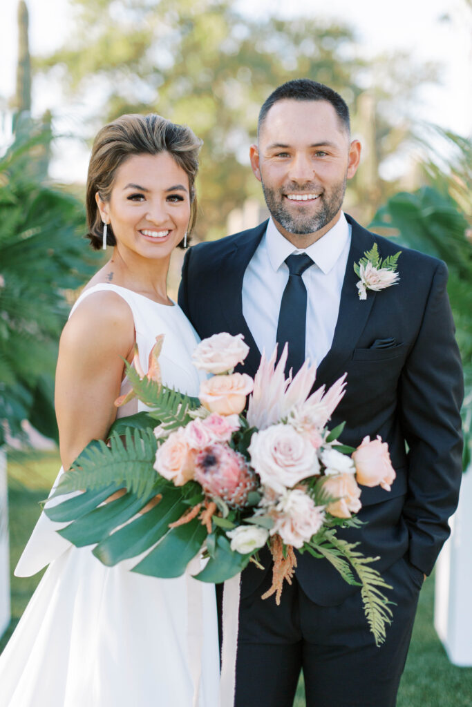 Bride and groom smiling, bride holding large tropical bouquet.