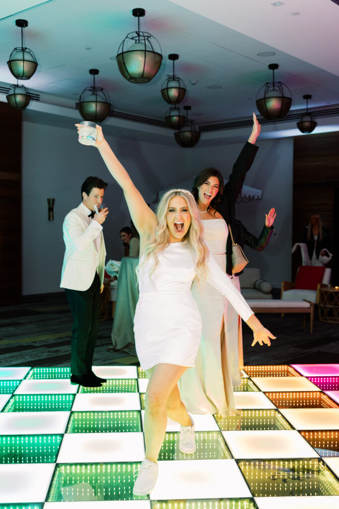 Two ladies dancing on a dance floor with a man in the background.