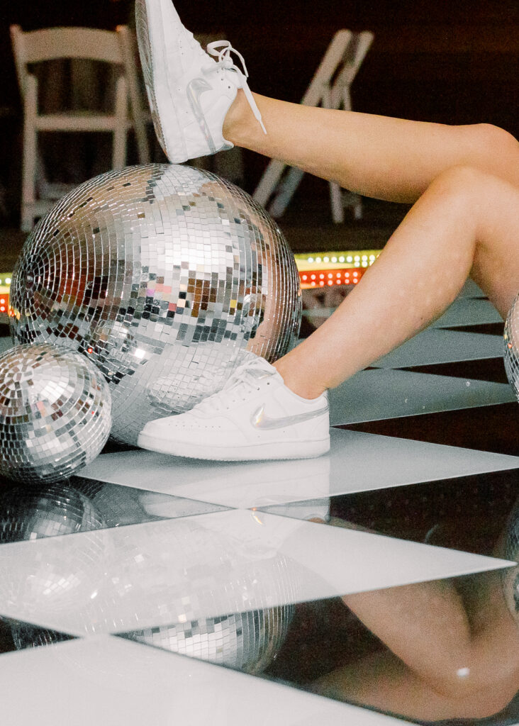 A woman sitting on a dance floor with her foot on a disco ball.
