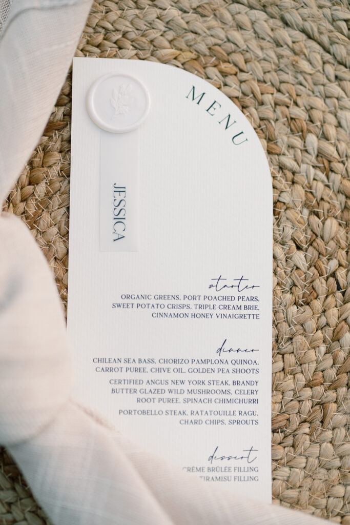 White wedding menu with a white seal on jute plate charger and a napkin.