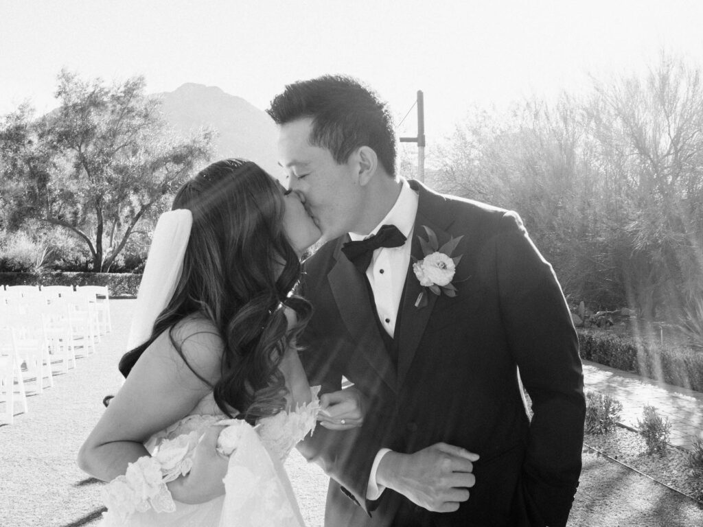 Black and white photo of bride and groom kissing at wedding ceremony.