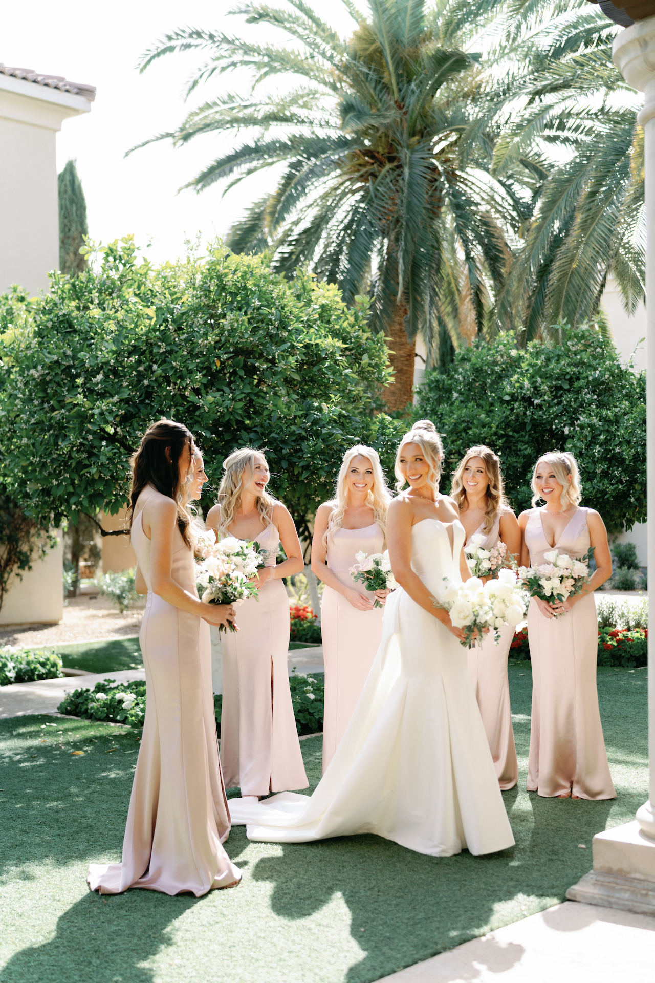 Bride with bridesmaids, all holding bouquets of flowers and smiling.
