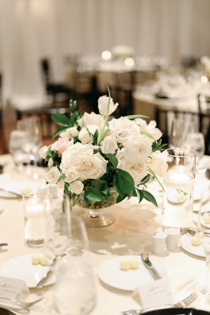 Wedding reception floral centerpiece of white and blush flowers in glass vase.