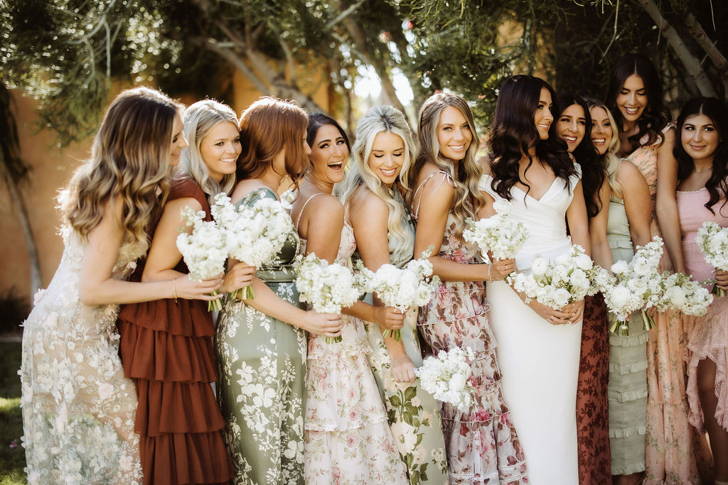 Bride standing in a row with bridesmaids in varied colors and patterns dresses.