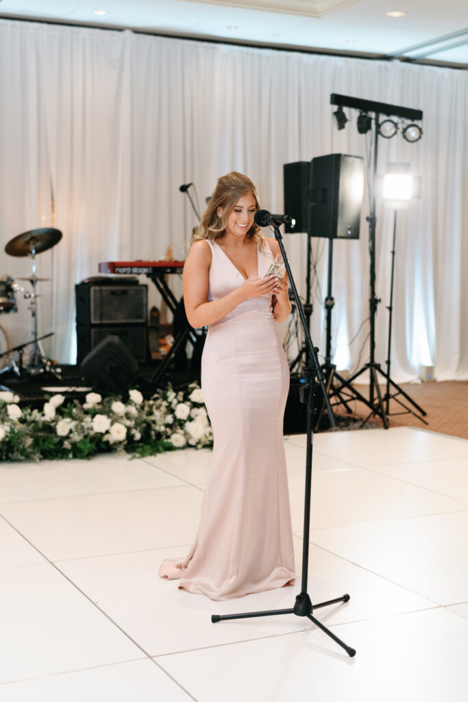 Bridesmaid at microphone on dance floor at wedding reception.