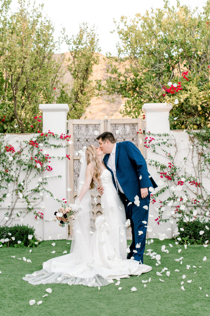 Bride and groom kissing in front of El Chorro doors with mountain views in background during white rose petal toss.