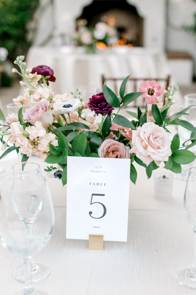 Wedding reception centerpiece on table of white linen with table number card in front of it.