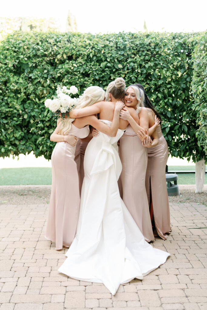 Bride hugging bridesmaids in dusty pink dresses in group.