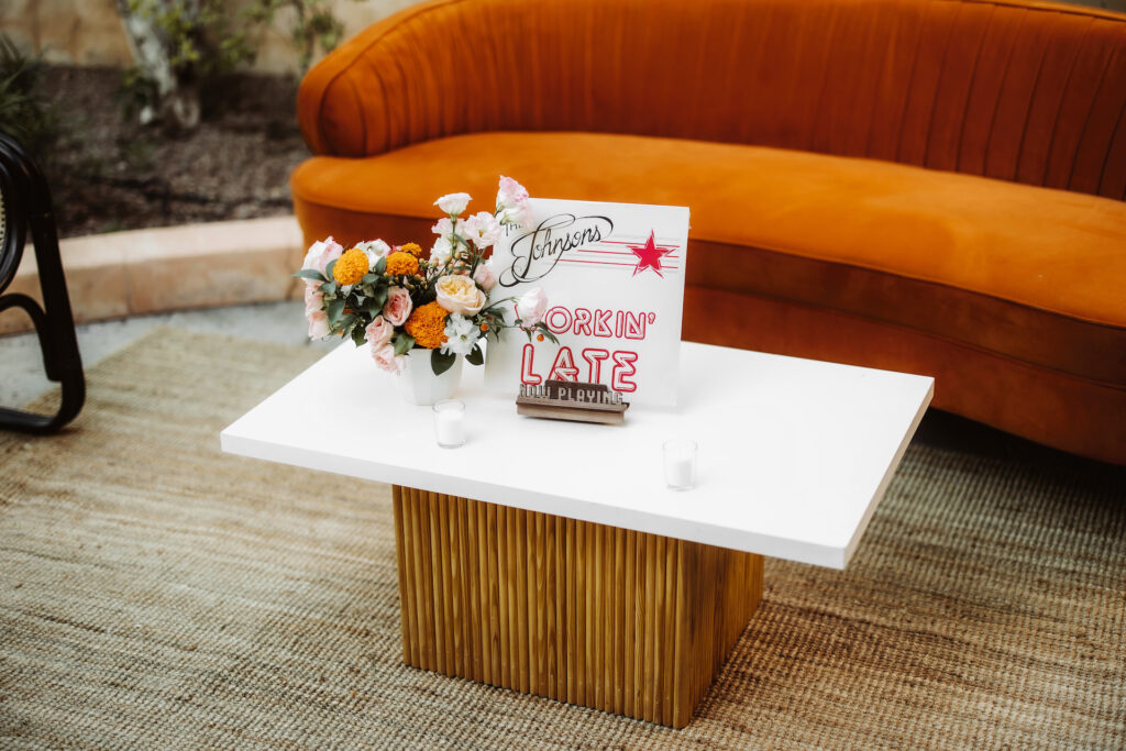Cocktail hour wedding space with copper colored couch and a coffee table with sign, votive candle, and floral arrangement.