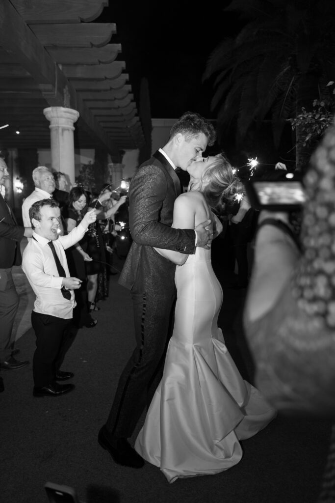 Bride and groom kissing outside in the dark with wedding guests holding sparklers around them.