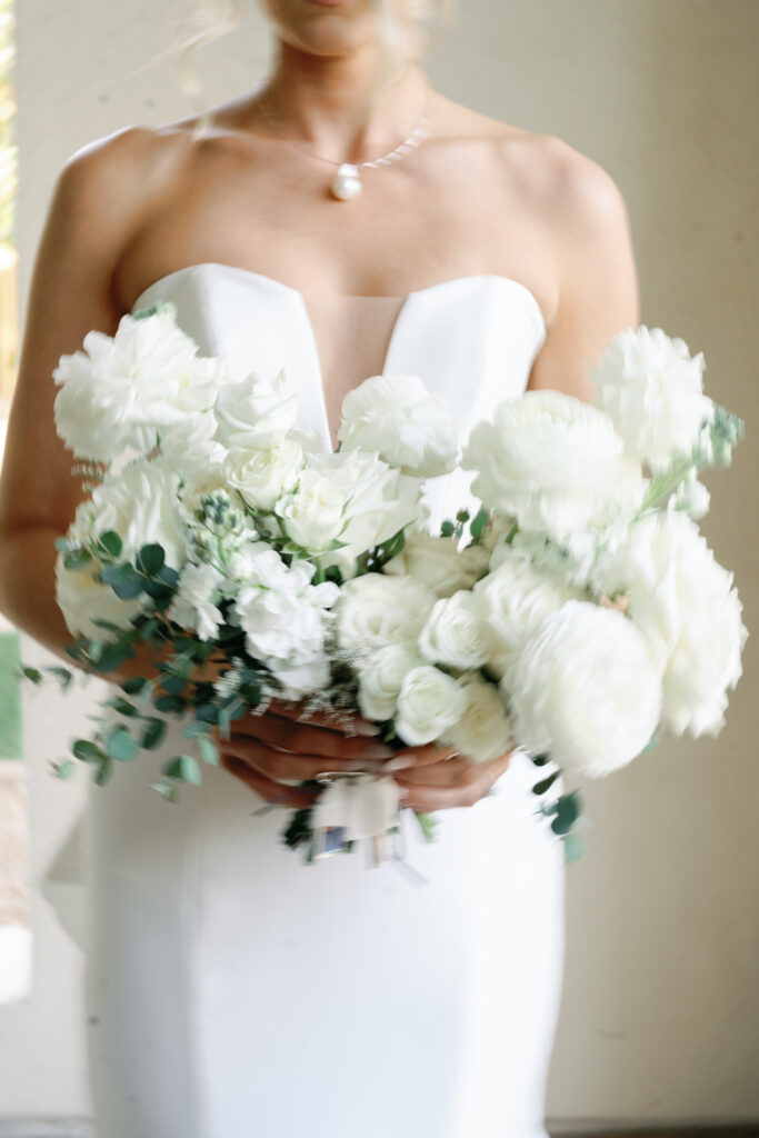 Bride holding bouquet of white flowers and greenery, including roses.