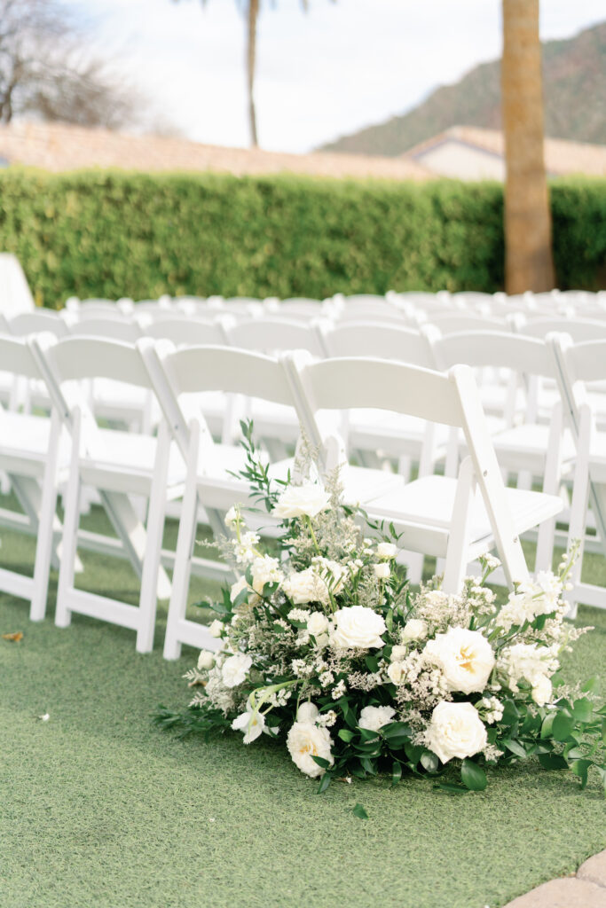 Ground floral arrangement of white flowers at wedding ceremony behind chair.