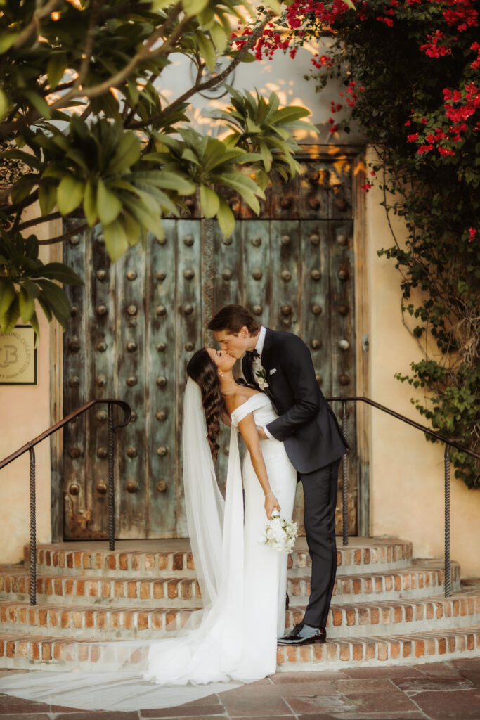Bride and groom kissing on steps of Royal Palms large double doors outside.