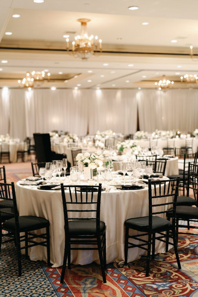 Wedding reception round tables with white linens and black chairs and white flower centerpieces.