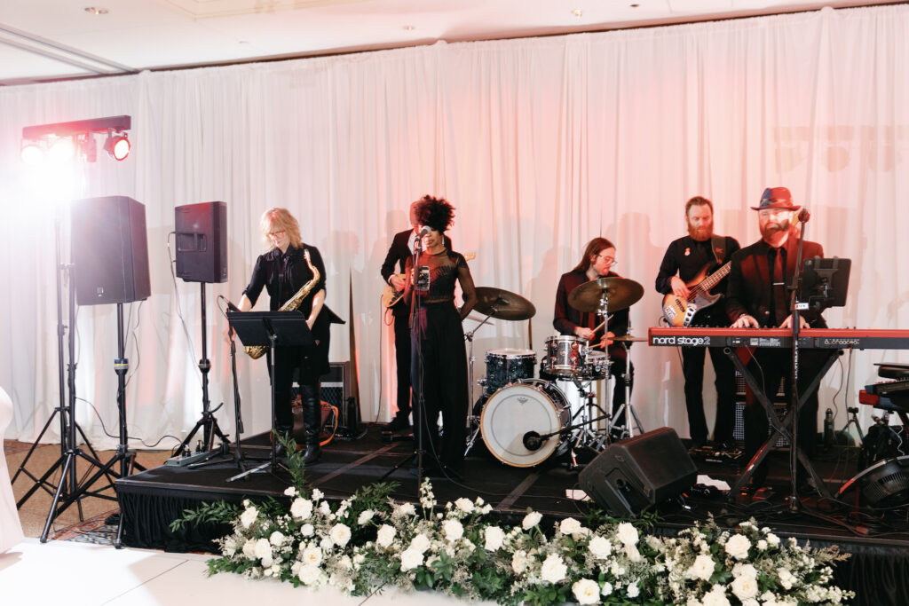 Live wedding band at reception with flowers on the ground in front of stage.