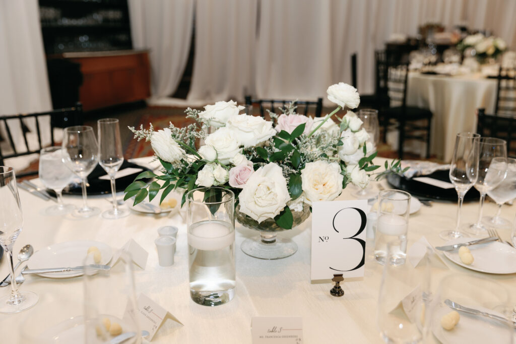 Wedding reception floral centerpiece of white and blush flowers in glass vase.