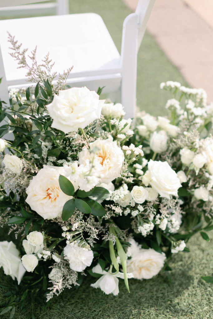 Ground floral arrangement of white flowers at wedding ceremony behind chair.